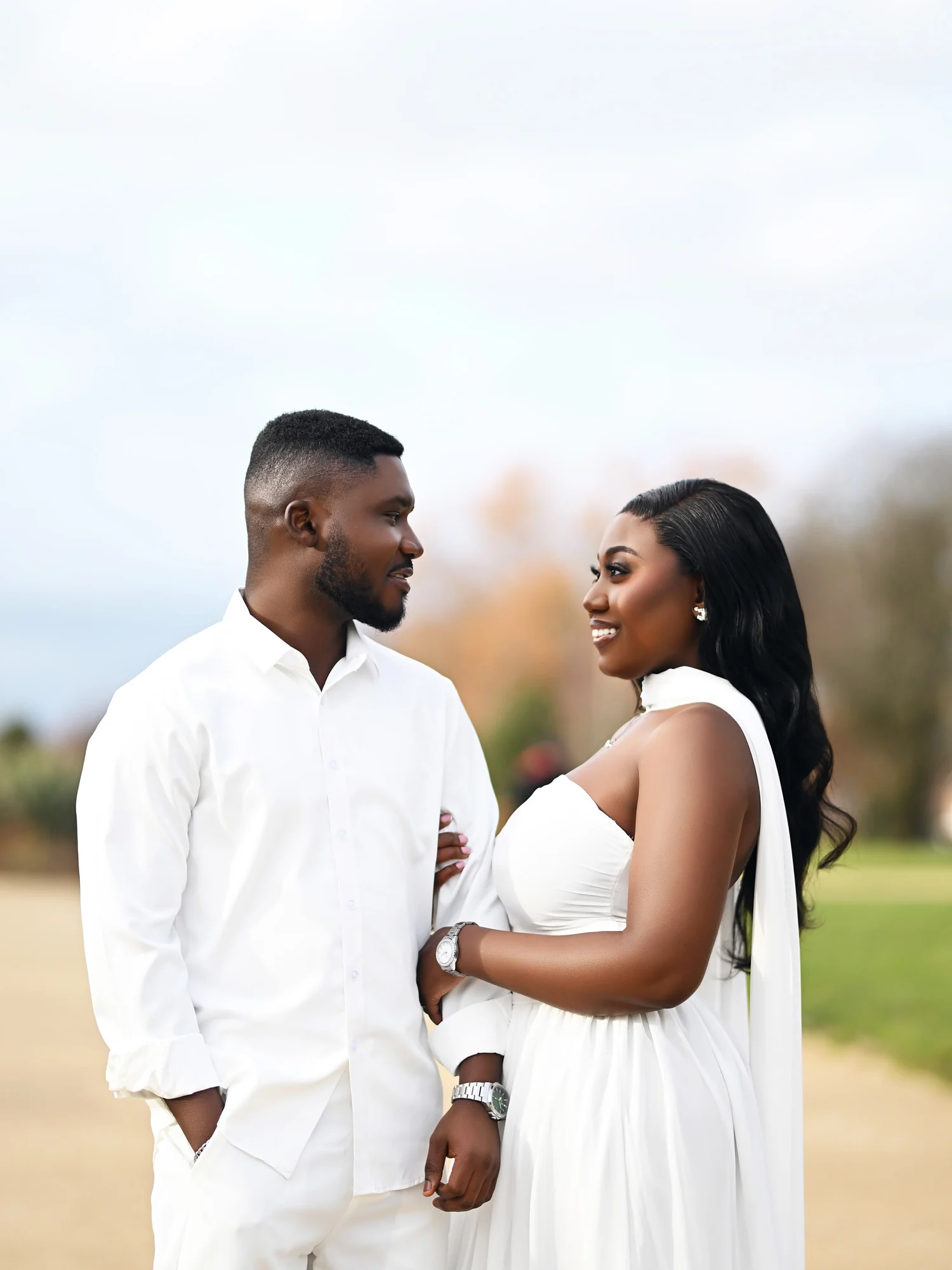 A couple dressed in white smiling at each other outdoors